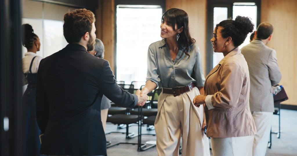 People, handshake and smile for seminar, talk and greeting for networking event, meeting or workshop. Happy, women and shaking hands with man, conference and discussion for collaboration and business